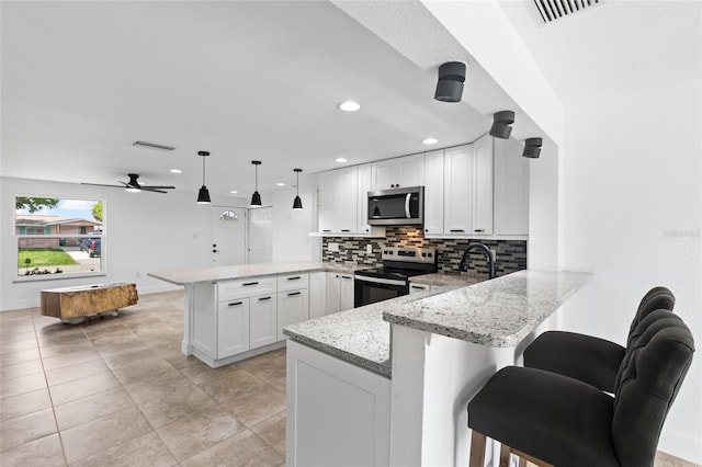 kitchen with appliances with stainless steel finishes, kitchen peninsula, pendant lighting, white cabinets, and a breakfast bar