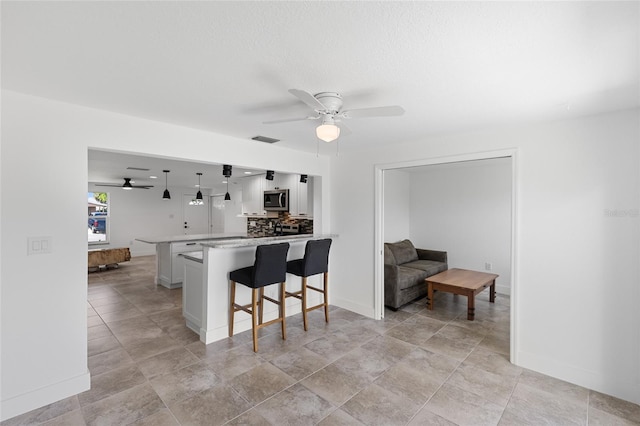 kitchen with kitchen peninsula, decorative backsplash, white cabinets, ceiling fan, and a kitchen bar