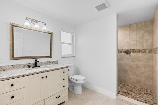 bathroom featuring vanity, toilet, a tile shower, and tile patterned flooring