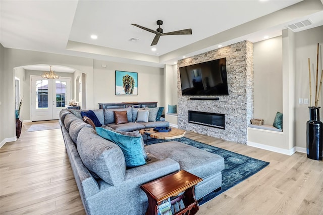 living room featuring a fireplace, light wood-type flooring, ceiling fan with notable chandelier, and a raised ceiling