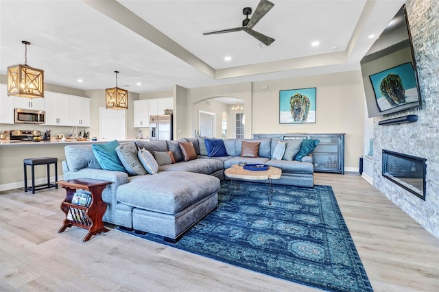 living room featuring ceiling fan, a fireplace, light hardwood / wood-style flooring, and a raised ceiling