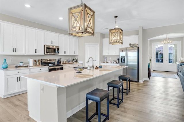 kitchen featuring stainless steel appliances, light hardwood / wood-style floors, decorative light fixtures, and an island with sink