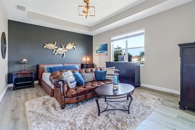 bedroom featuring light hardwood / wood-style floors, a notable chandelier, and a raised ceiling