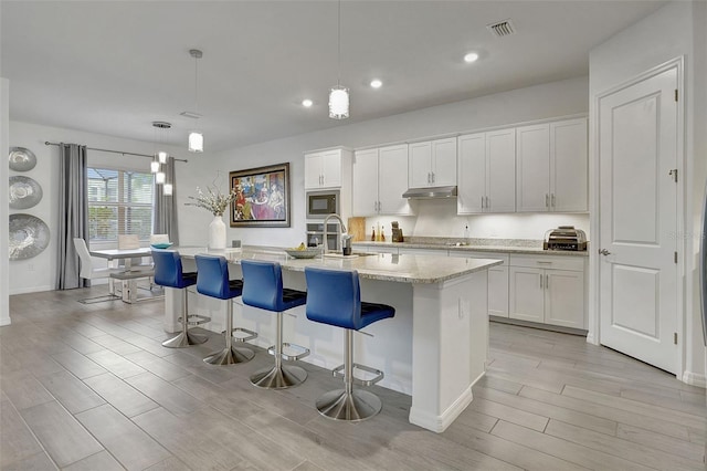 kitchen featuring a kitchen island with sink, hanging light fixtures, white cabinetry, and black appliances