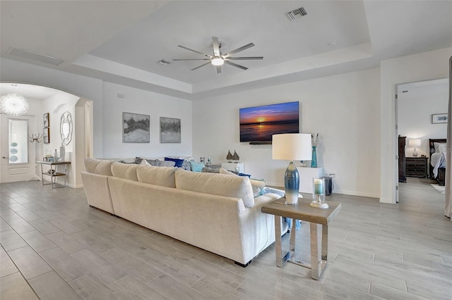 living room with a raised ceiling and ceiling fan