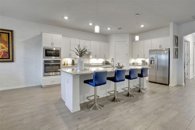 kitchen with stainless steel appliances, a kitchen island with sink, pendant lighting, and white cabinets