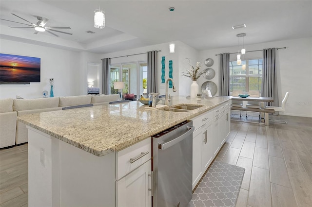 kitchen with pendant lighting, dishwasher, sink, white cabinets, and a center island with sink