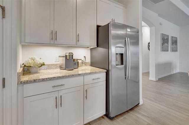 kitchen featuring light stone counters, white cabinetry, stainless steel fridge, and light hardwood / wood-style flooring