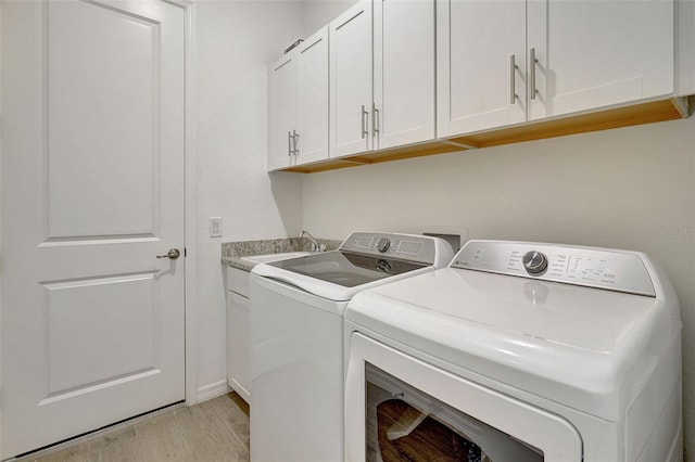 laundry room featuring sink, light hardwood / wood-style flooring, washing machine and dryer, and cabinets