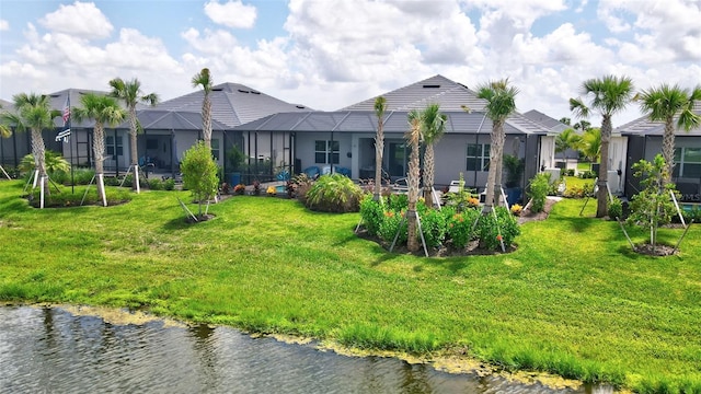 back of property with a water view, a yard, and glass enclosure