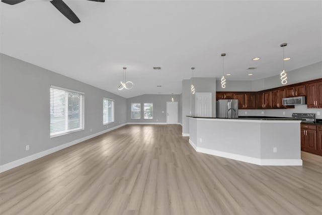 kitchen featuring baseboards, open floor plan, appliances with stainless steel finishes, light wood-type flooring, and dark countertops