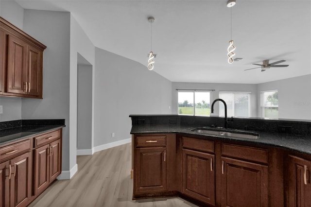 kitchen with light wood finished floors, dark stone countertops, a sink, and decorative light fixtures