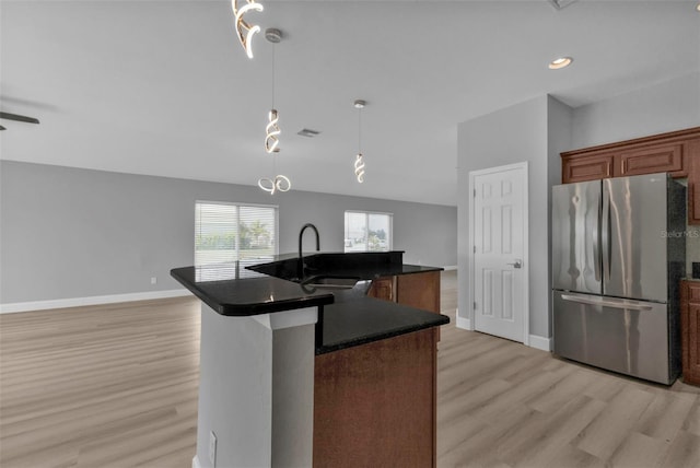 kitchen with a sink, baseboards, light wood-style floors, freestanding refrigerator, and dark countertops