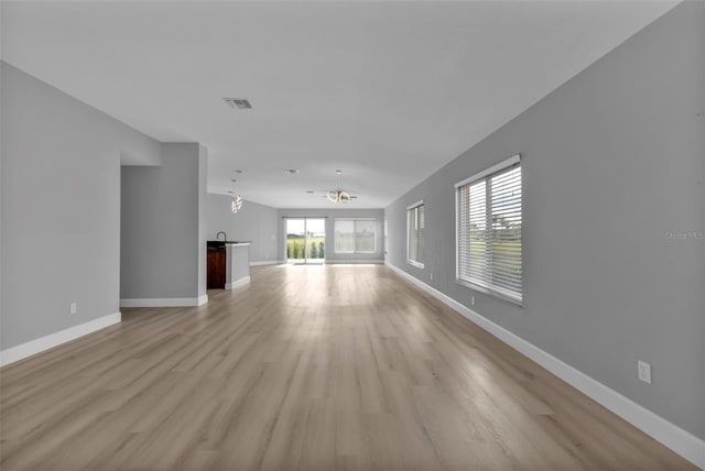 unfurnished living room featuring baseboards, visible vents, light wood finished floors, and an inviting chandelier