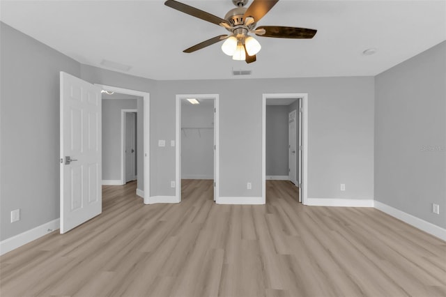 unfurnished bedroom featuring light wood finished floors, baseboards, visible vents, and a walk in closet