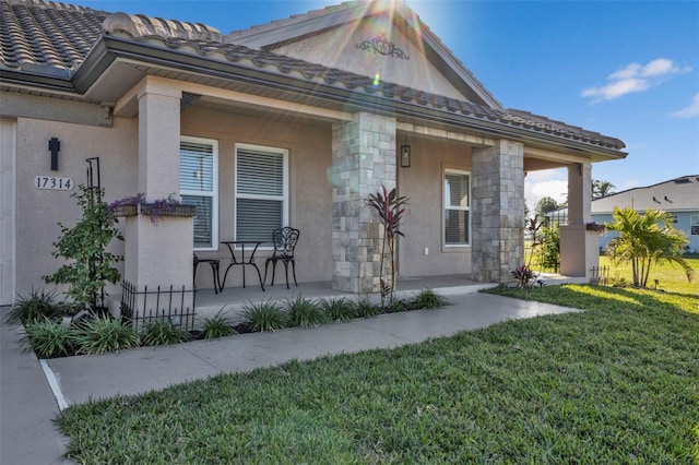 exterior space with stone siding, a tile roof, a yard, a porch, and stucco siding