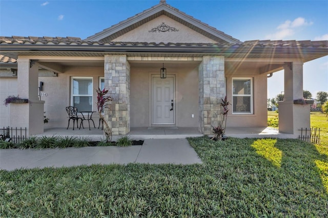 doorway to property with a porch, stone siding, a tiled roof, and stucco siding