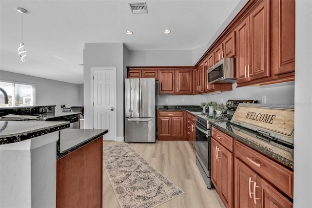 kitchen with visible vents, hanging light fixtures, appliances with stainless steel finishes, light wood-type flooring, and dark stone countertops