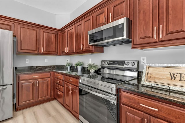 kitchen with light wood-style flooring, appliances with stainless steel finishes, and dark stone counters