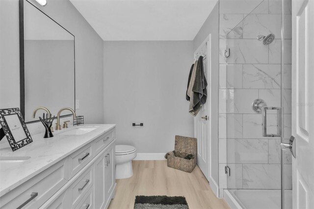 full bathroom with double vanity, a stall shower, baseboards, wood finished floors, and a sink