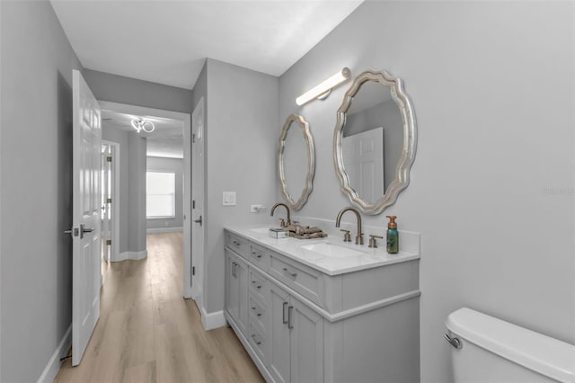 bathroom with double vanity, baseboards, toilet, wood finished floors, and a sink