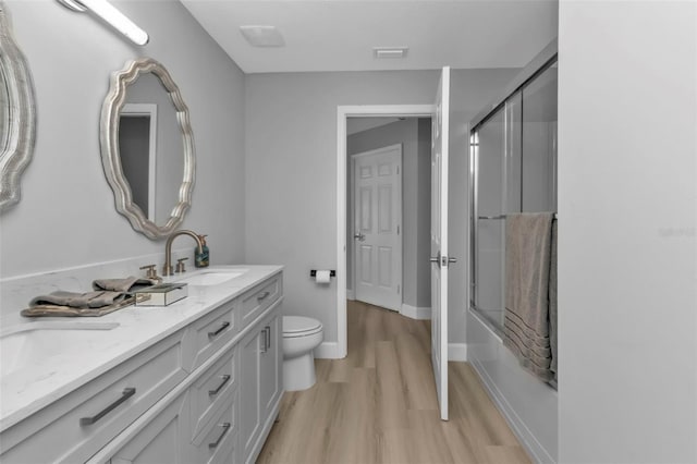 full bathroom featuring enclosed tub / shower combo, toilet, wood finished floors, visible vents, and a sink