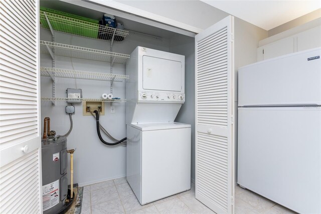 clothes washing area featuring stacked washing maching and dryer, light tile patterned floors, and water heater