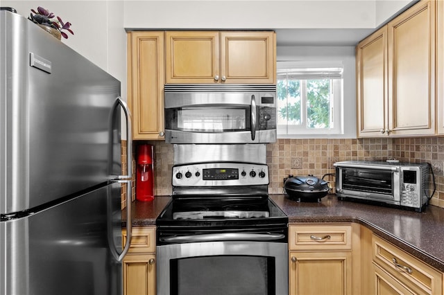 kitchen featuring light brown cabinets, dark countertops, backsplash, appliances with stainless steel finishes, and a toaster