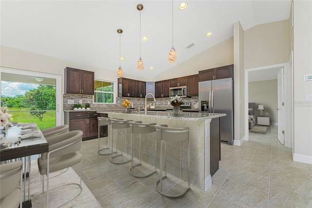 kitchen featuring light tile patterned flooring, tasteful backsplash, an island with sink, appliances with stainless steel finishes, and decorative light fixtures