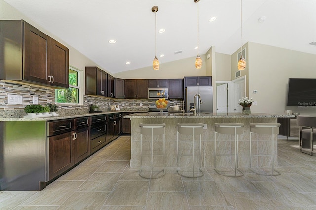 kitchen featuring stainless steel appliances, sink, backsplash, light tile patterned floors, and an island with sink