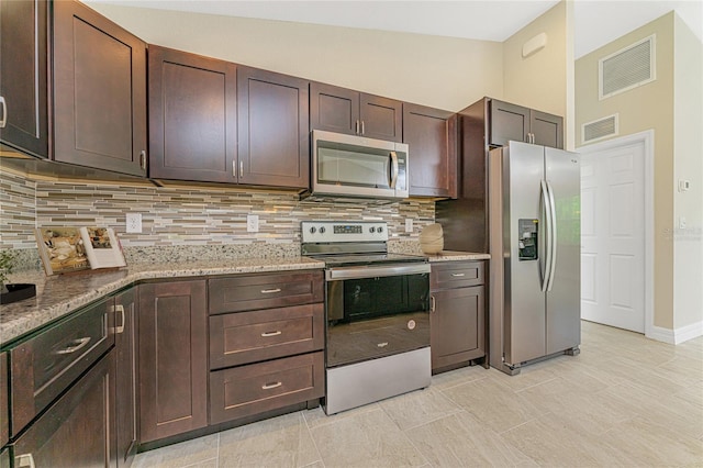 kitchen with stainless steel appliances, light stone counters, lofted ceiling, light tile patterned floors, and backsplash