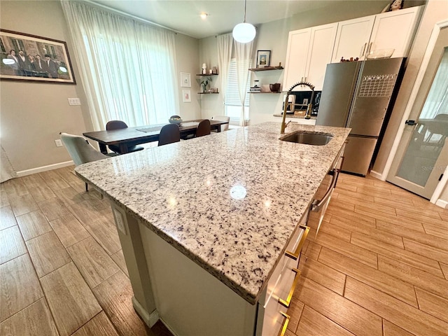 kitchen with pendant lighting, stainless steel refrigerator, sink, white cabinets, and light stone counters