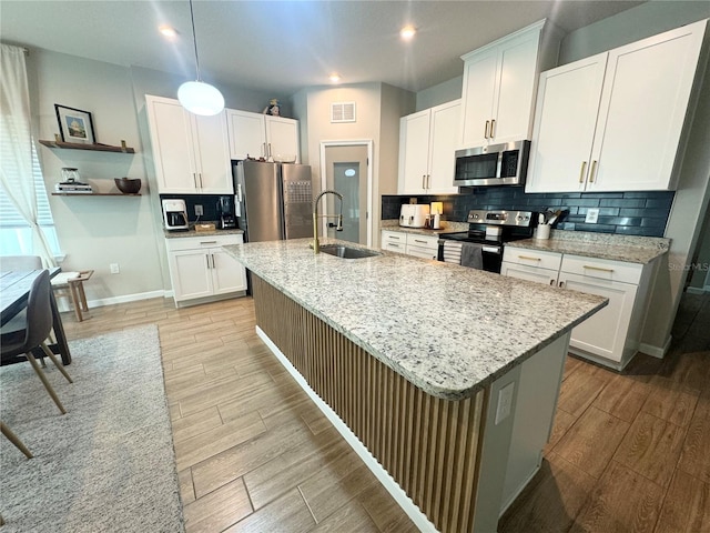 kitchen featuring sink, appliances with stainless steel finishes, white cabinetry, light stone countertops, and an island with sink