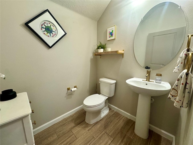 bathroom with toilet, sink, wood-type flooring, vaulted ceiling, and a textured ceiling