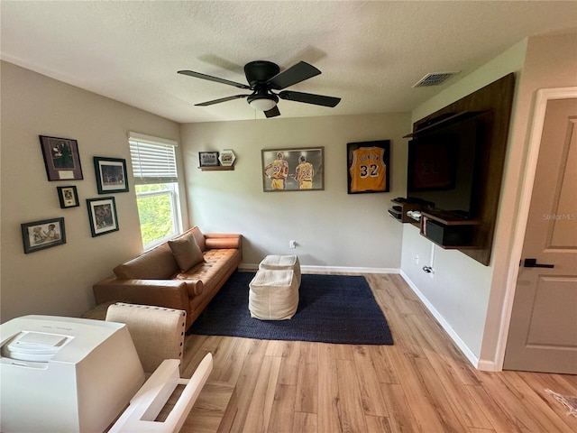 living room featuring ceiling fan, a textured ceiling, and light wood-type flooring