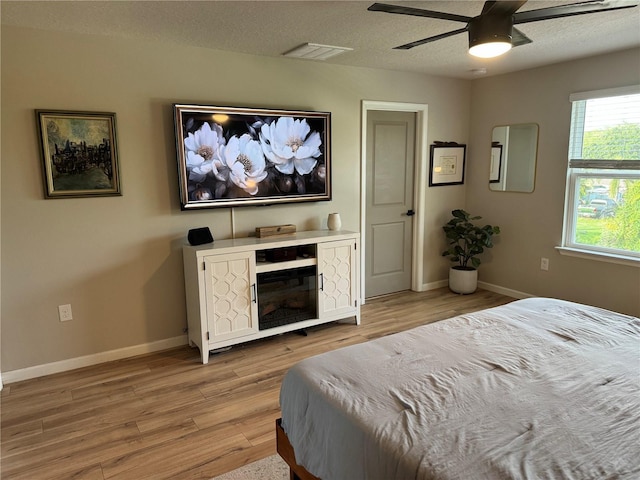 bedroom with ceiling fan, light hardwood / wood-style flooring, and a textured ceiling