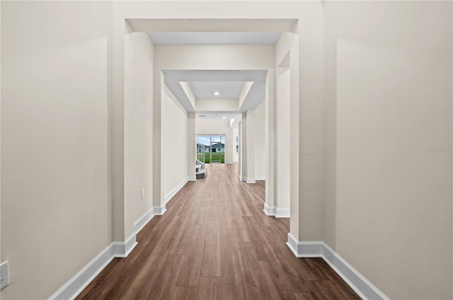 corridor with a raised ceiling and dark wood-type flooring