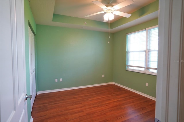 unfurnished bedroom featuring ceiling fan, a raised ceiling, dark wood finished floors, and baseboards