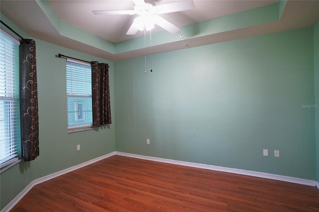 spare room with ceiling fan, wood finished floors, a raised ceiling, and baseboards