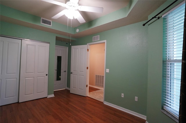 unfurnished bedroom with ceiling fan, a tray ceiling, and dark hardwood / wood-style floors