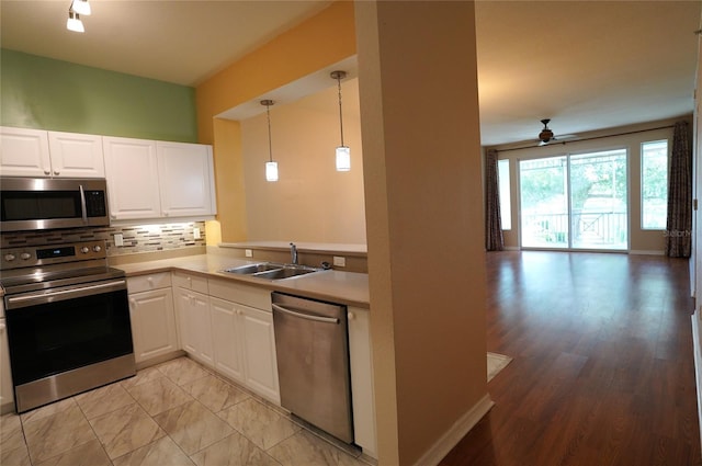 kitchen featuring stainless steel appliances, a sink, white cabinetry, open floor plan, and tasteful backsplash