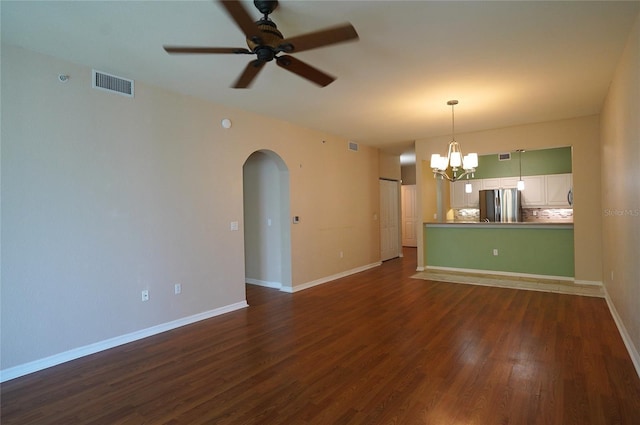 interior space featuring arched walkways, dark wood-style flooring, visible vents, baseboards, and ceiling fan with notable chandelier