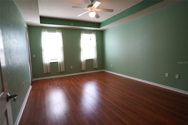 empty room with ceiling fan, baseboards, a raised ceiling, and wood finished floors