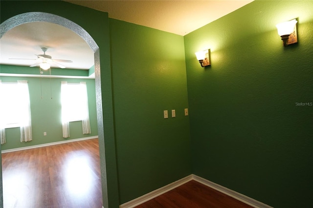 spare room featuring arched walkways, ceiling fan, baseboards, and wood finished floors