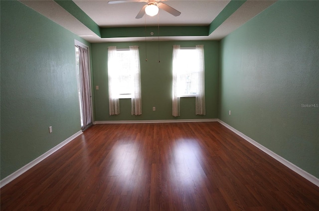 unfurnished room with a tray ceiling, ceiling fan, and dark hardwood / wood-style flooring