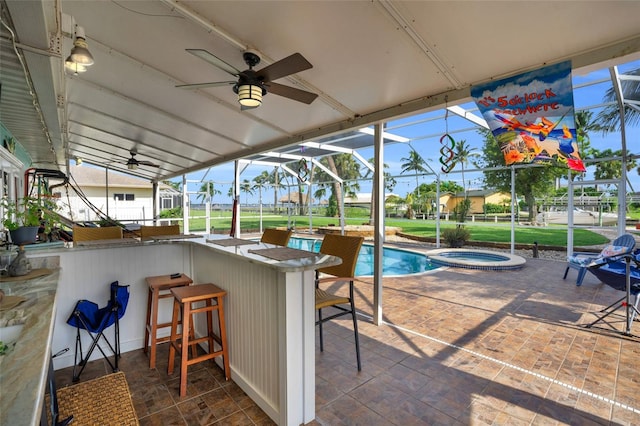 view of swimming pool with an in ground hot tub, an outdoor bar, a patio, glass enclosure, and ceiling fan