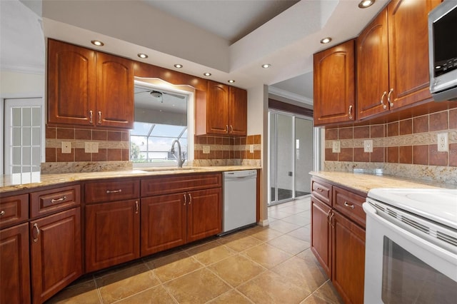 kitchen featuring sink, crown molding, tasteful backsplash, white appliances, and light stone countertops