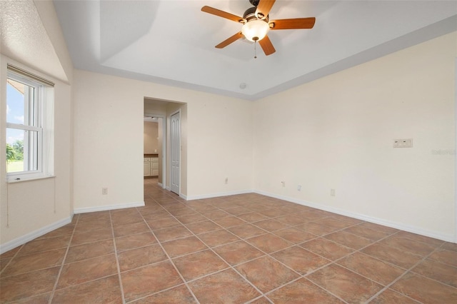 tiled empty room with a tray ceiling and ceiling fan