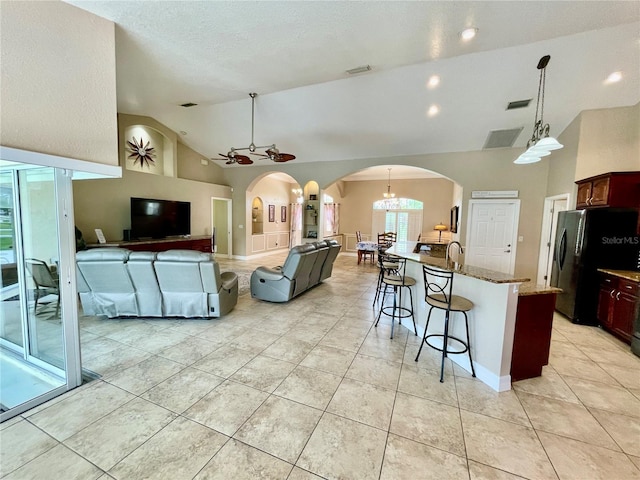 kitchen featuring stone counters, stainless steel fridge, a kitchen bar, hanging light fixtures, and light tile patterned floors