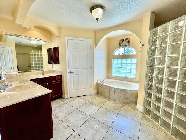 bathroom featuring tile patterned flooring, vanity, tiled bath, and a textured ceiling